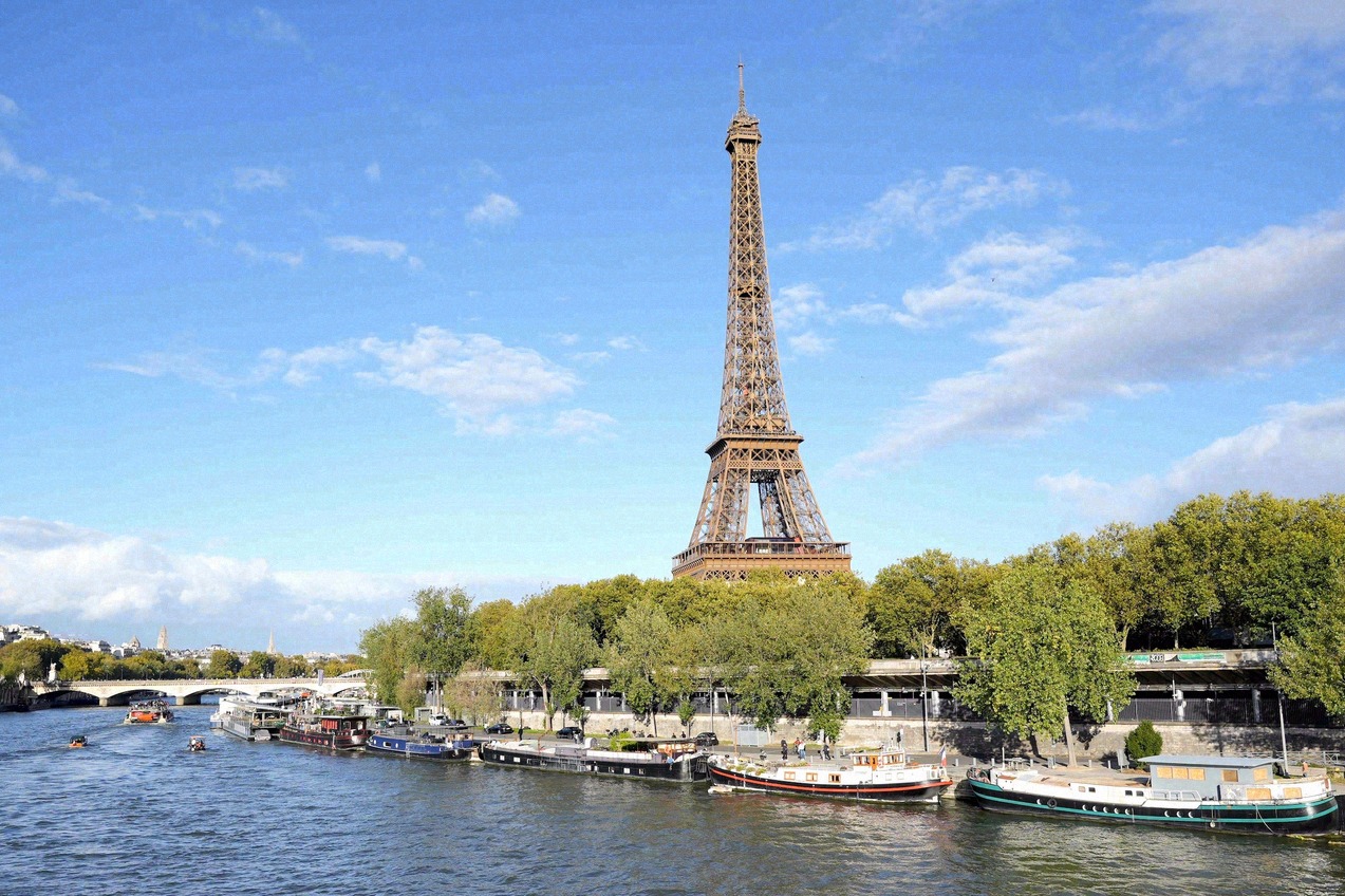 The Eiffel Tower seen from the Seine, with houseboats moored along the bank